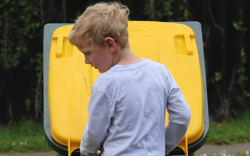 Boy taking a yellow-lid recycling bin to the kerb for collection.